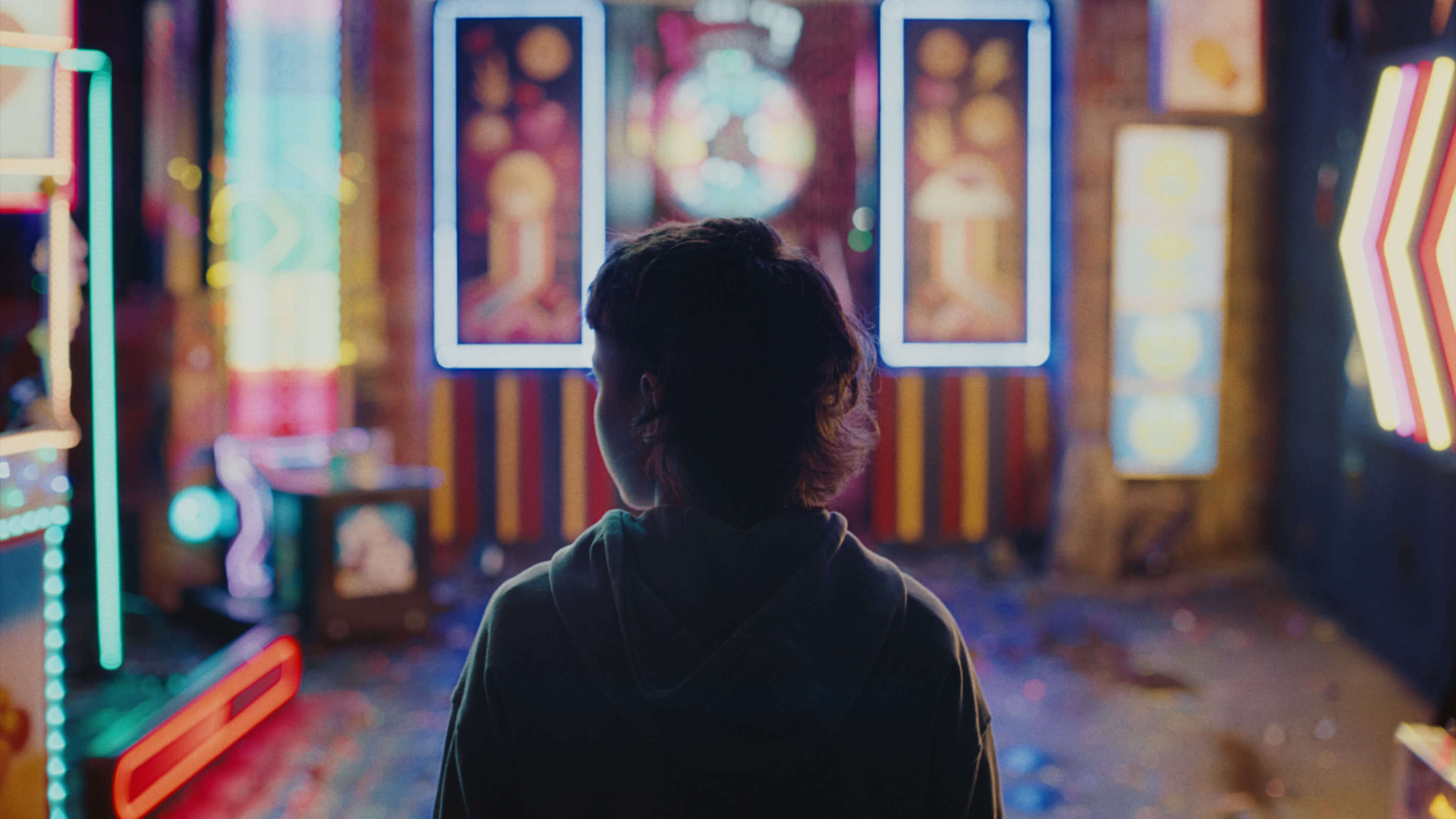 An image of a young boy facing away from the camera, appearing in an arcade of bright lights