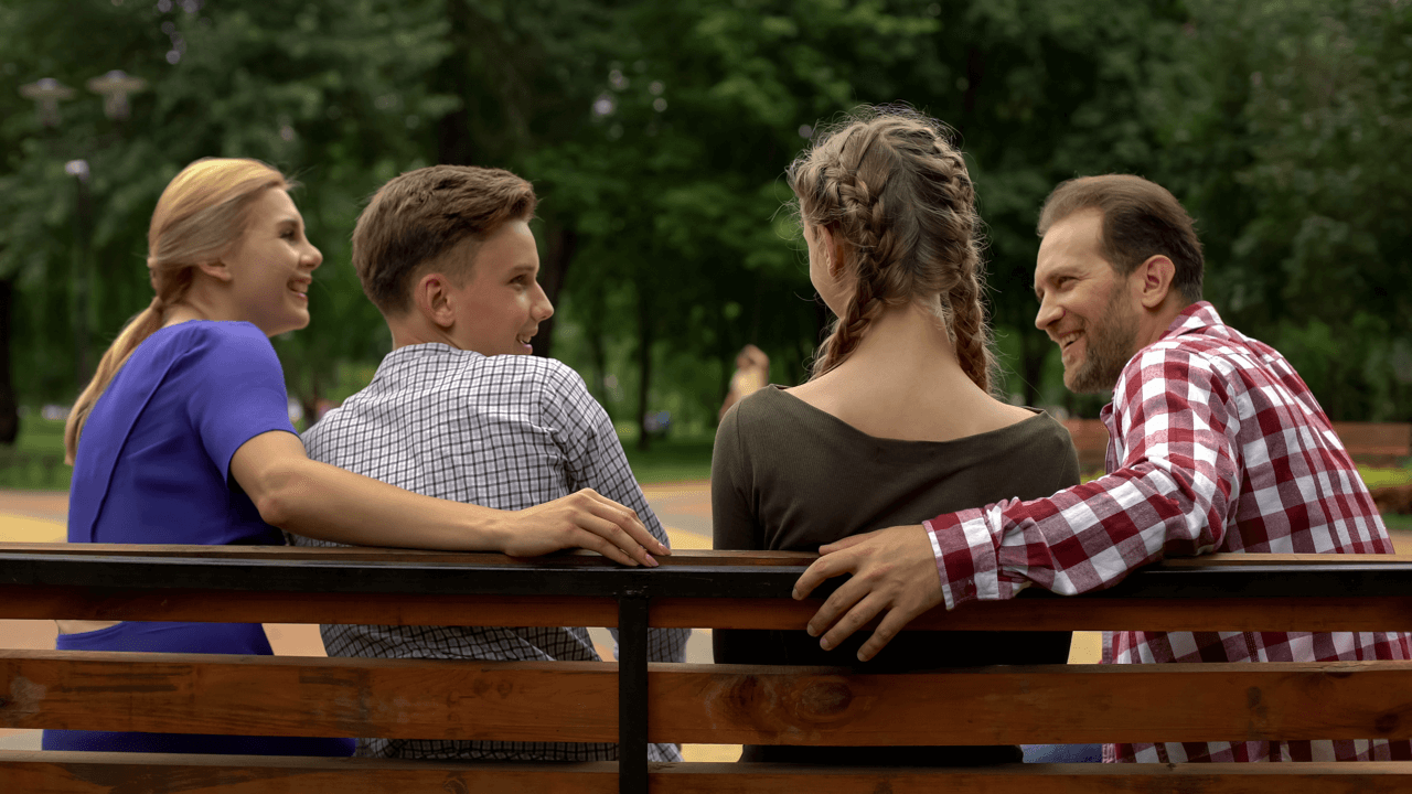 An image of a family sitting on a bench, talking and smiling