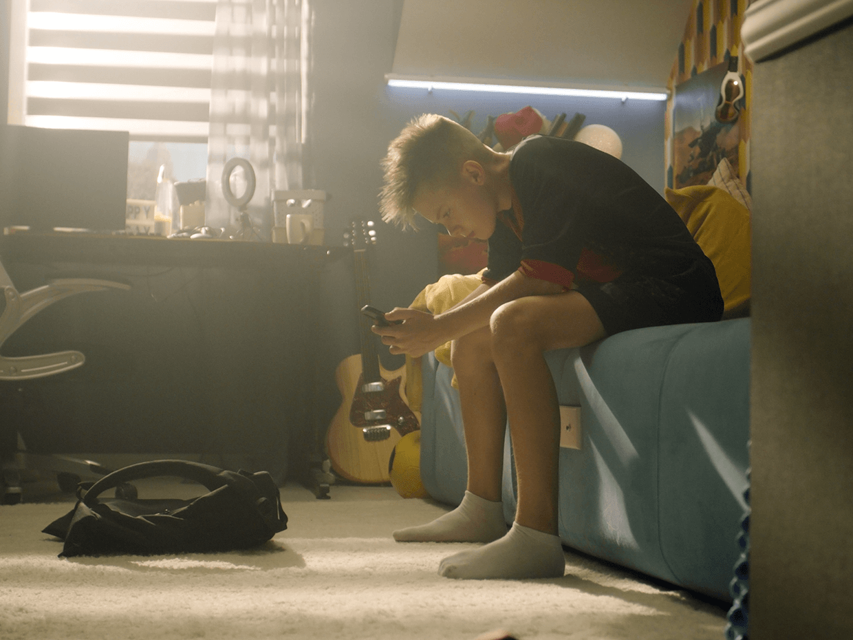 A boy sitting on a blue couch, looking at his phone.